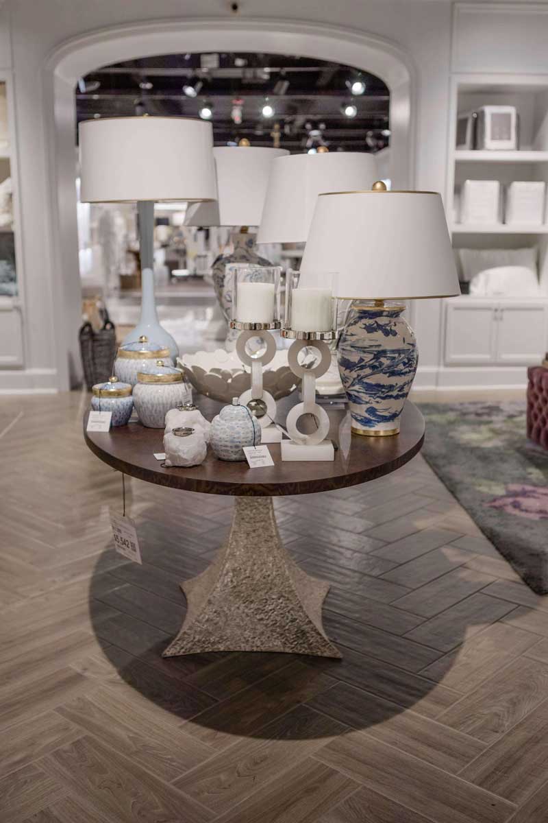 A round wooden table with several lamps, candle holders, and decorative pots and vases